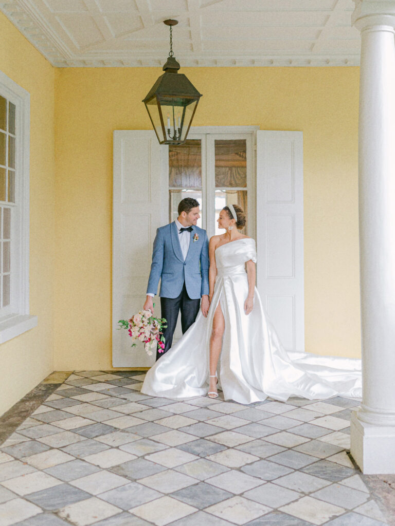 a man in tuxedo  and woman in wedding dress looking at each other smiling. Standing in a doorway at the William Aiken House Wedding venues in Charleston, SC