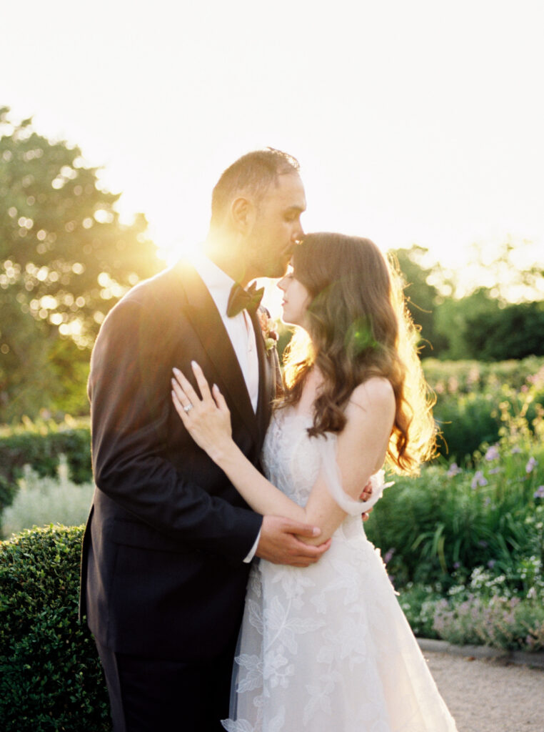 Eolia Mansion Destination wedding with bridal couple in an embrace with groom kissing his brides forehead at sunset with the glow of the sun behind them 