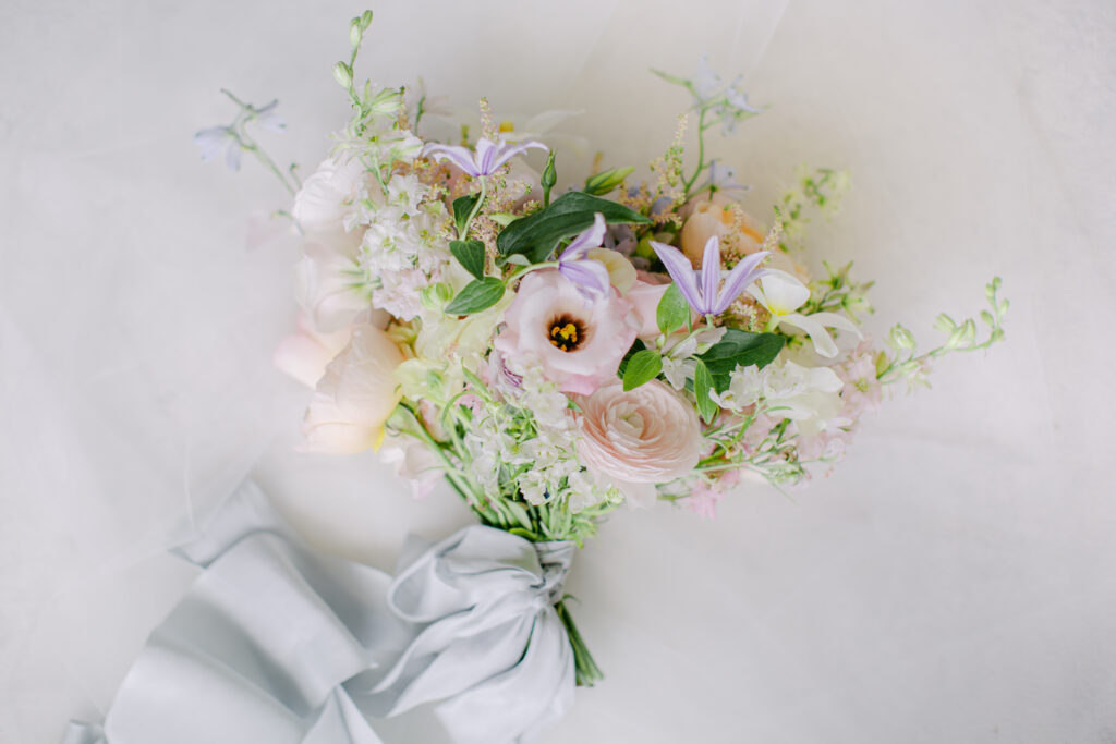 Garden Bouquet in colors of pinks, peach, purples and white with ranunculus, pastel roses wrapped in pastel blue silk ribbon.