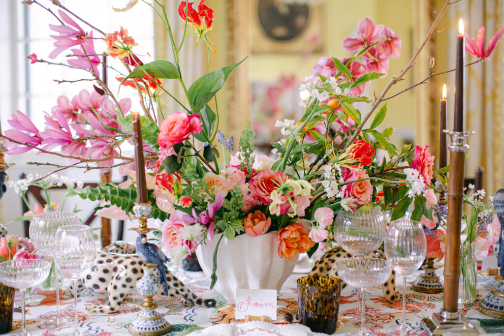 Wedding Venue Lowndes Grove in Charleston. Inside the Yellow room with jungle themed wedding reception. Centerpiece with hues of pinks, hot pinks and magentas fuschias. Brown and silver candle sticks with blue parrots and a tiger. 