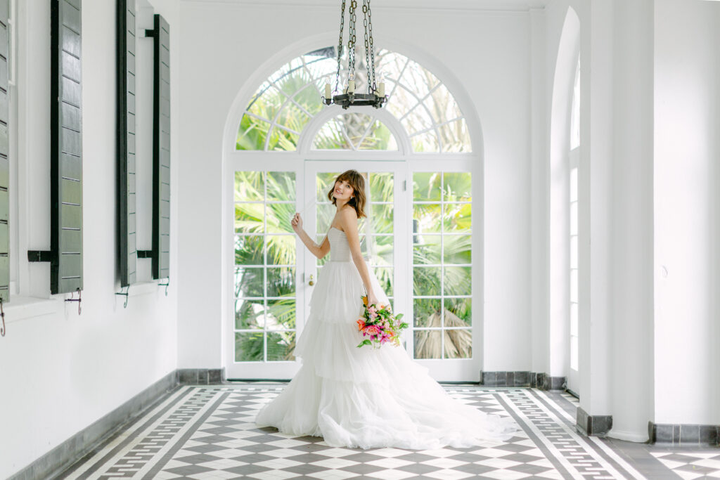 a woman in a white wedding dress holding a bouquet of flowers in the foyer of lowndes grove estate.