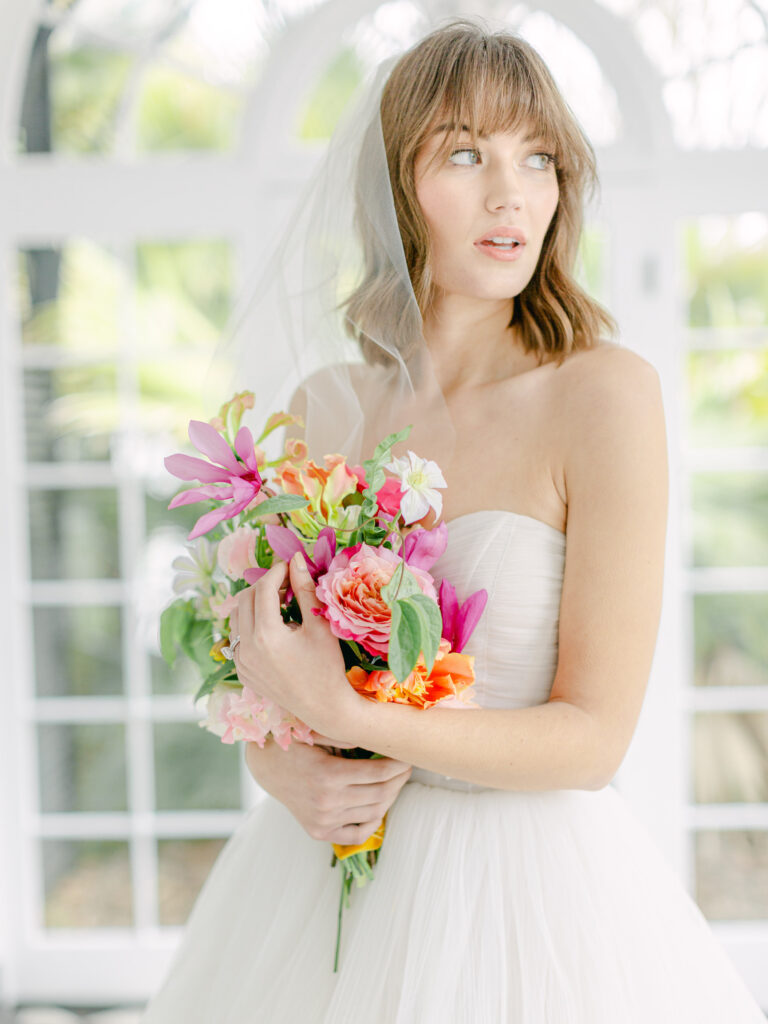 Close up of bride looking out the window in a soft romantic look. She's holding a jungle tropical inspired bouquet of flowers. View from inside the vestibule at Lowndes Grove for a destination wedding