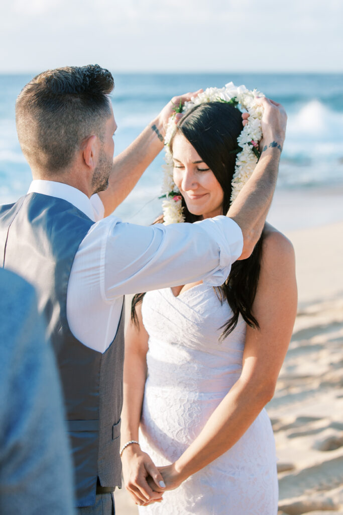 a man putting a flower lei over a woman's head on the beach in Hawaii.