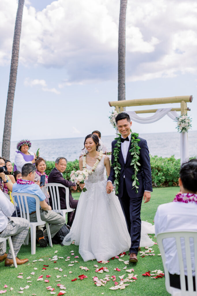 a man and woman walking down a aisle holding hand after wedding ceremony at paradise cove hawaii