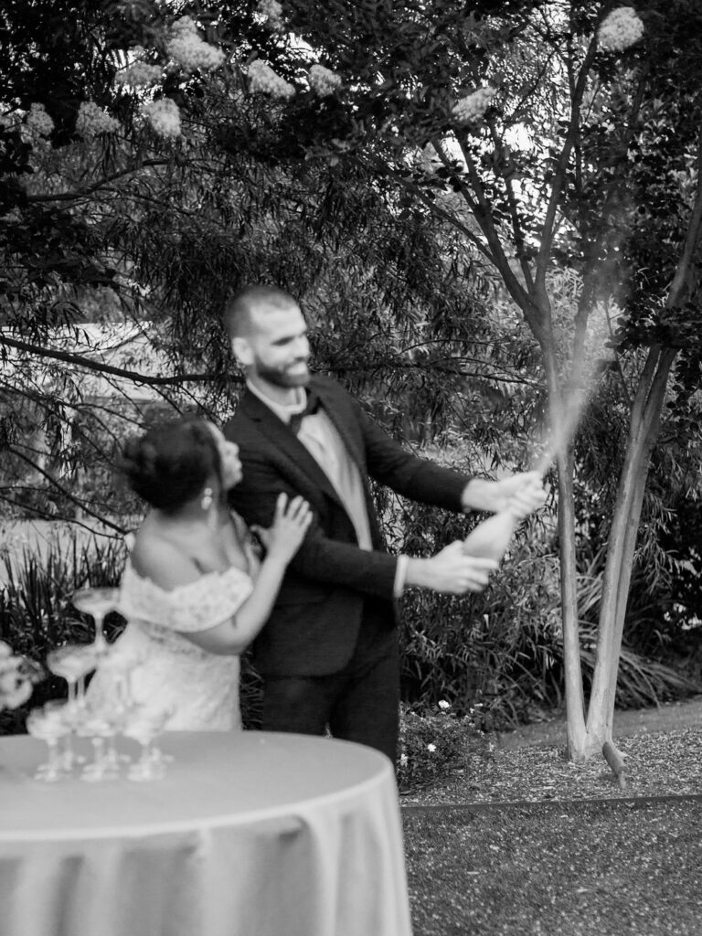 A Joyful Summer Wedding at a Private Estate in Raleigh, NC 8 Man and woman popping a bottle of champagne bottle ata raleigh nc wedding venue