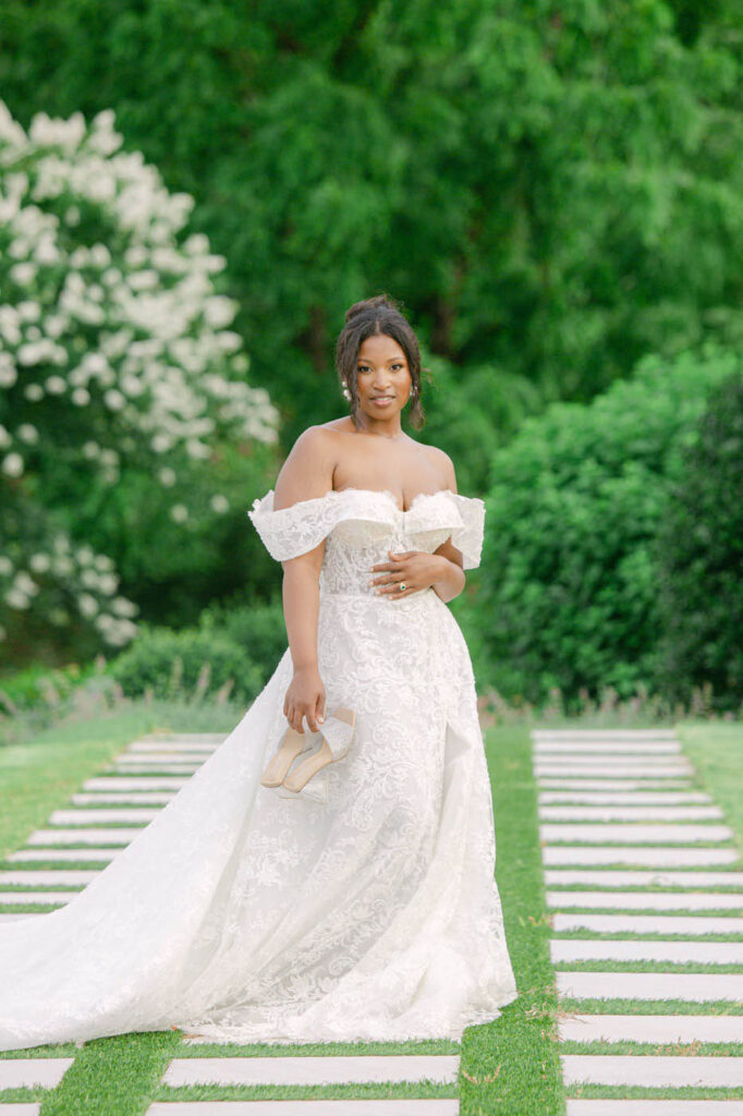 A Joyful Summer Wedding at a Private Estate in Raleigh, NC 4 A woman in a wedding gown holding shoes and looking at the camera at a wedding in Raleigh NC